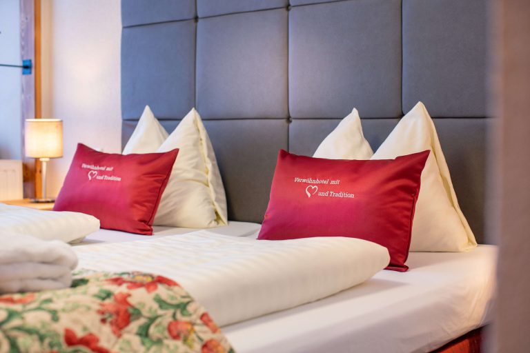Gemütliche Zimmer im Vötter's Hotel mit roten Kissen und Bergblick.