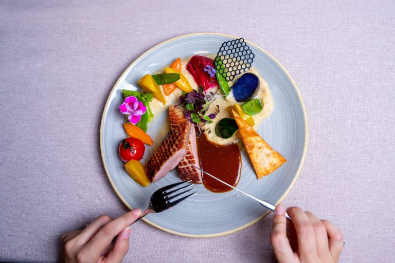 Futuristisch angerichteter Teller mit Fleisch, Gemüse und Soße, dekoriert mit essbaren Blumen.