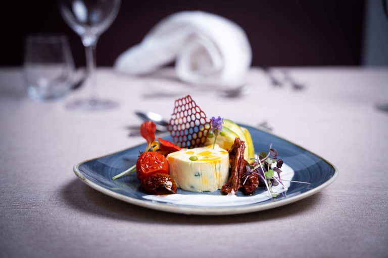 Kreativ angerichtetes Gericht mit Gemüse, Käse und Dekoration auf blauem Teller.